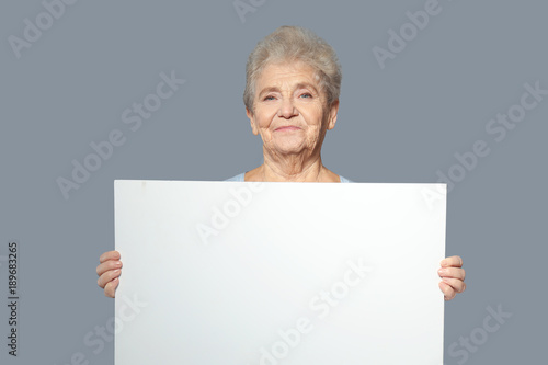 Senior woman with blank advertising board on grey background
