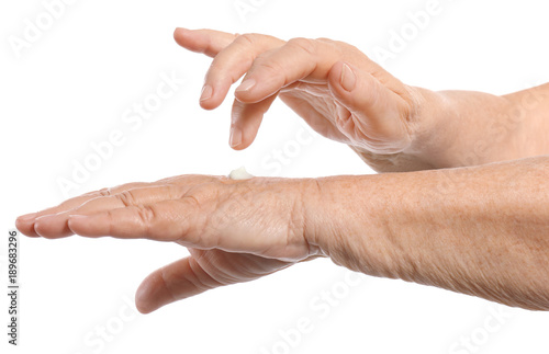 Senior woman applying hand cream, on white background