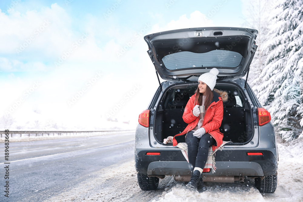 Naklejka premium Female tourist drinking tea near car in snowy countryside