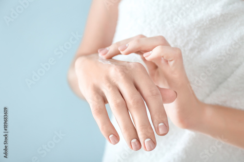Young woman applying hand cream on color background, closeup