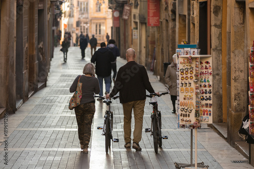 Fototapeta Naklejka Na Ścianę i Meble -  Mature couple of cyclist travelers strolling through European picturesque city.