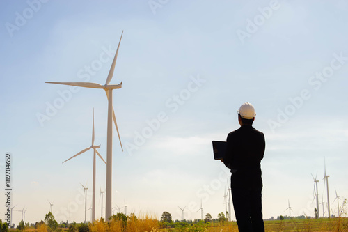 Portrait of engineer asian man holding laptop with the wind turbine in background.