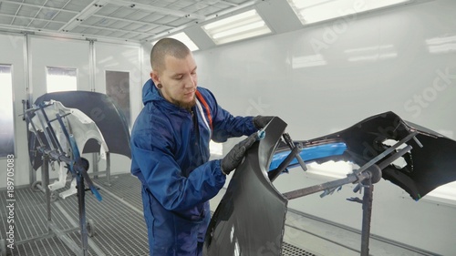 Serviceman preparing a car bodykit for painting in a workshop