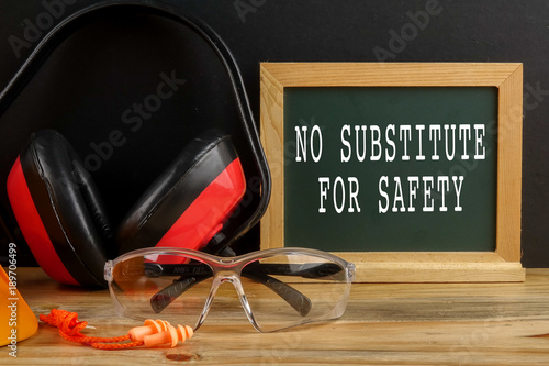 HEALTH AND SAFETY CONCEPT. Personal protective equipment on wooden table over black background with NO SUBSTITUTE FOR SAFETY TEXT photo