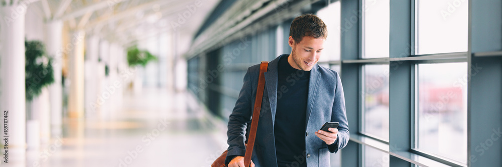 Smiling man looking at smart phone in airport - obrazy, fototapety, plakaty 