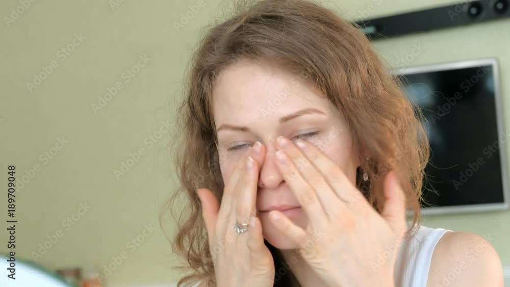 Young woman putting on mascara and looking in hand mirror in bedroom at home Young woman putting on mascara and looking in hand mirror in bedroom at home