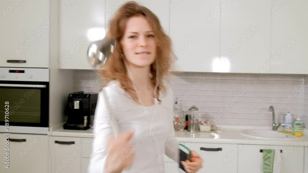 Happy curly haired girl dancing in kitchen wildly hair bouncing dress at home having wild fun listening to music Happy curly haired girl dancing in kitchen wildly hair bouncing dress at home having wild fun listening to music