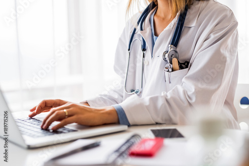 Female doctor with laptop working at the office desk. Fototapeta
