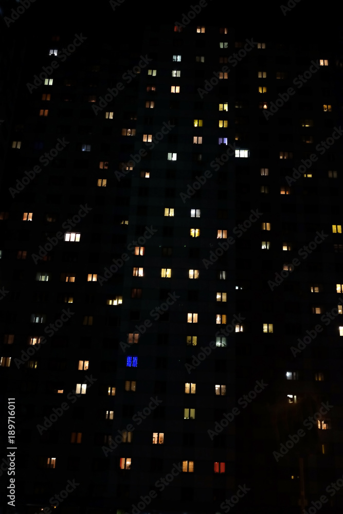 Facade of large multi-storey block of flats with many bright lighting windows in apartments front view at night