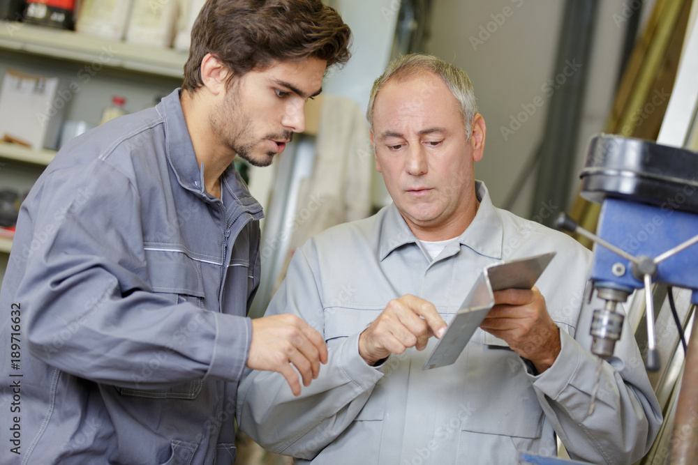 Obraz premium Workers by bench drill looking at shaped metal