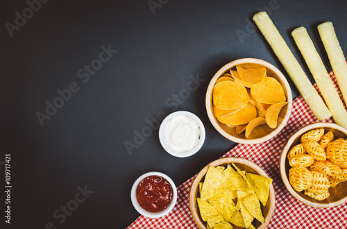 Party snacks - potato chips and snacks in bowl on black slate table. Photograph taken from above, top view with copy space around products.