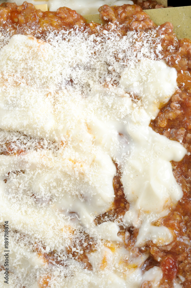 Fototapeta premium How to cook Italian lasagna,vertical background with close up on a raw italian lasagna, from above. ready to be baked, with ragu, bechamel grated cheese.