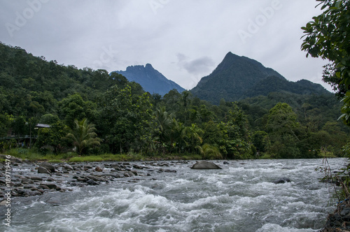 The Kedamaian River rushing streadily past the Tambatuon Homestead Viewing Platform. Can be seen here the twin Mount Kinabalu and Mount Nungkok. photo