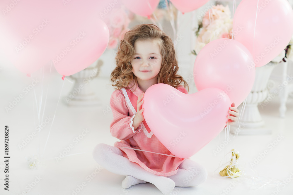 A little girl of 6 years with long curly hair,a beautiful smile, sits alone in a large bright room with lots of pink balloons in the shape of a heart. Valentine's Day and party celebration. A little girl of 6 years with long curly hair,a beautiful smile, sits alone in a large bright room with lots of pink balloons in the shape of a heart. Valentine's Day and party celebration.