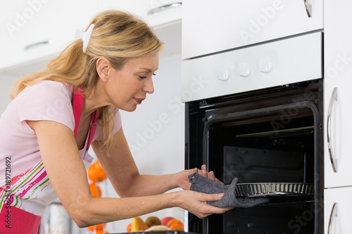 pretty blond woman putting tart in the oven for baking