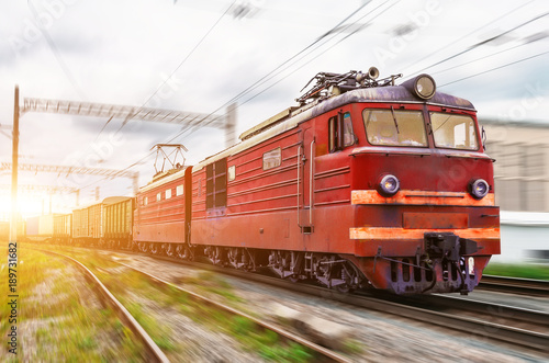 Red locomotive electric with a freight train at high speed rides by rail.
