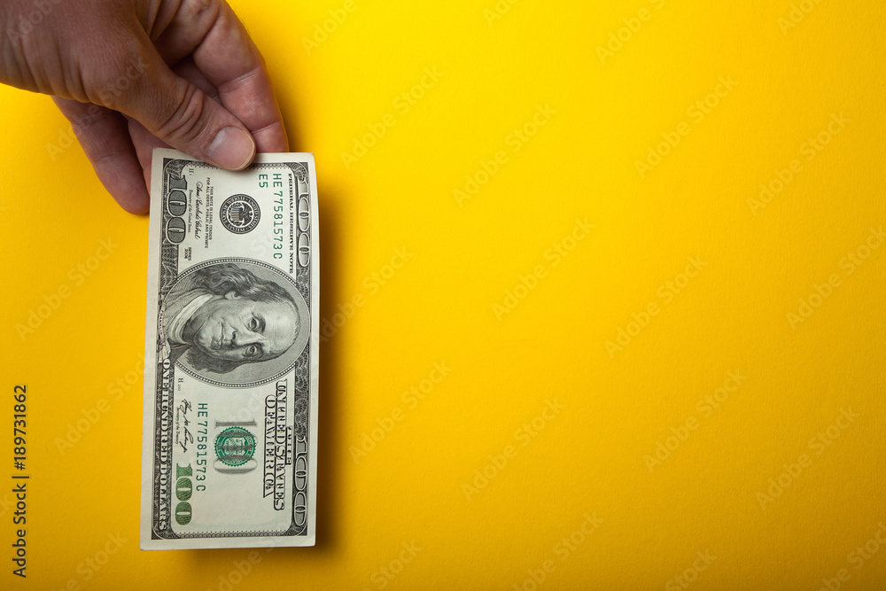A hundred dollars in hand on a yellow background, empty space for text. A hundred dollars in hand on a yellow background, empty space for text.