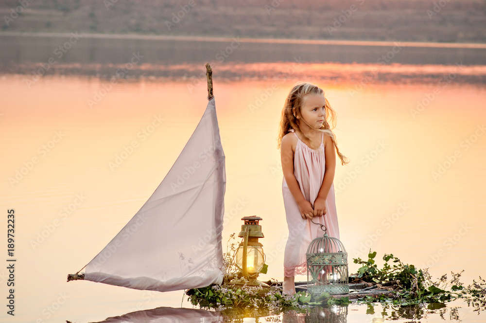 A little girl in a light dress sails at sunset