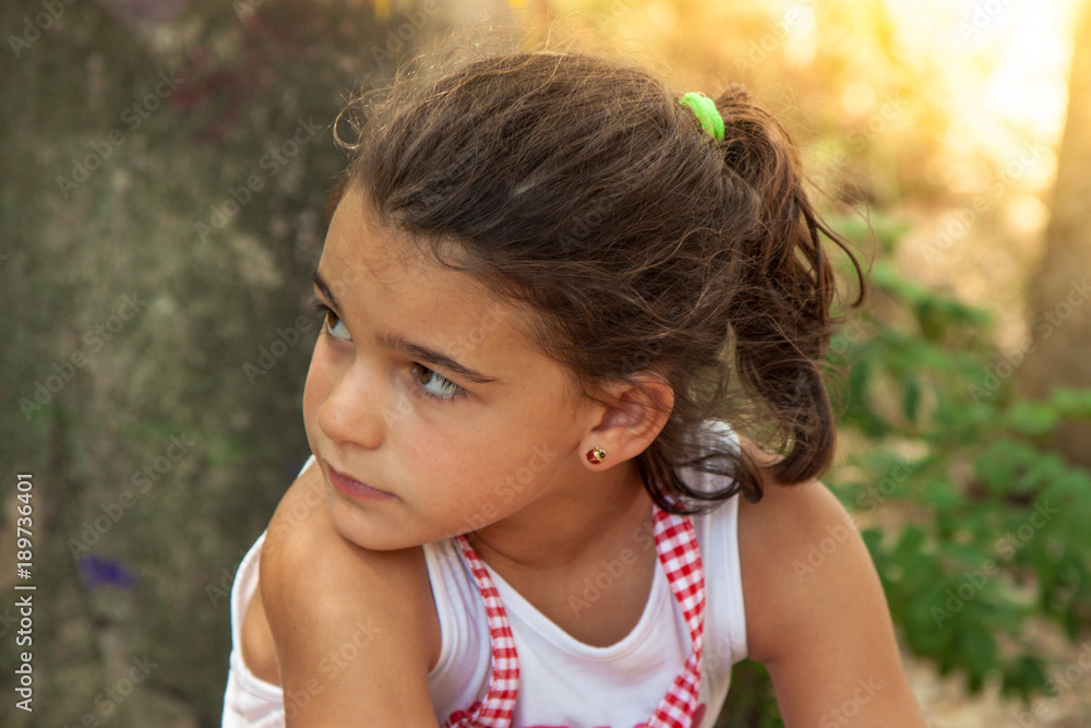 Young girl sitting leaning back against a tree in a park on a sunny summer day. Golden lens flare. Young girl sitting leaning back against a tree in a park on a sunny summer day. Golden lens flare.