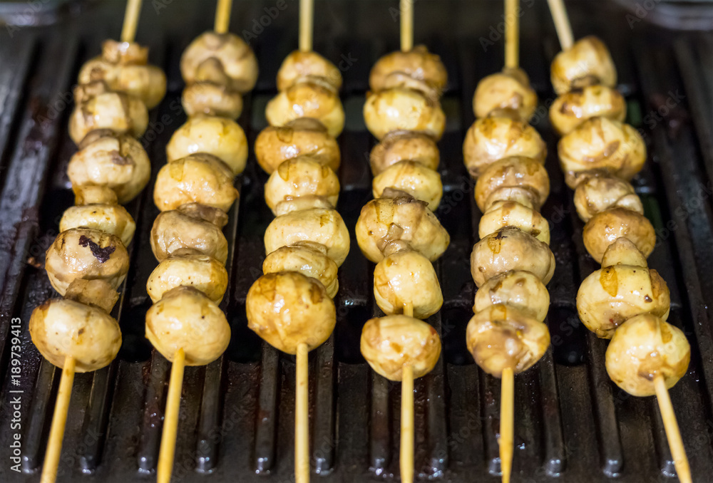 baked roast whole champignon on a wooden stick skewer against the background of a metal lattice bbq, a row of appetizing vegetables baked roast whole champignon on a wooden stick skewer against the background of a metal lattice bbq, a row of appetizing vegetables