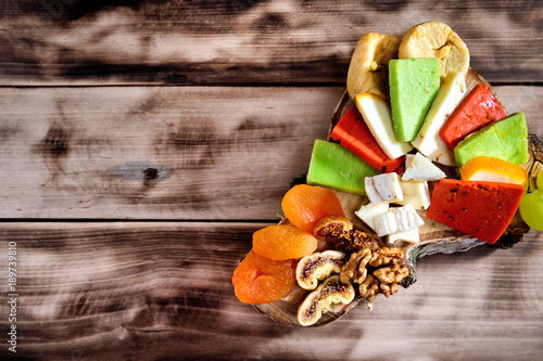 Various types of cheese, grapes, dried apricots, nuts and figs on a wooden cut on dark wooden background with copy space.