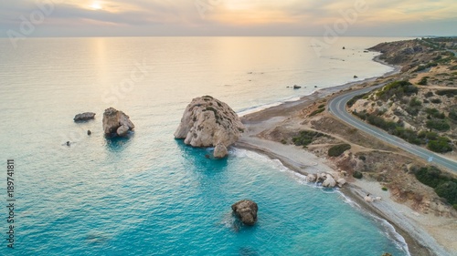 Aerial Bird's eye view of Petra tou Romiou, aka Aphrodite's rock a famous tourist travel destination landmark in Paphos, Cyprus. The sea bay of goddess Afroditi birthplace at sunset from above.  photo