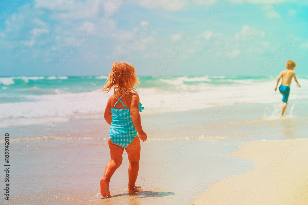 Fototapeta premium little girl and boy run play with waves on beach