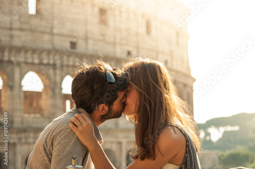 Photography Romantic happy couple young tourists in love kissing cuddling in front of colosseum in rome at sunset with lens flare