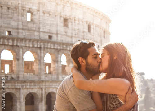 Photography Romantic happy couple young tourists in love kissing cuddling in front of colosseum in rome at sunset with lens flare