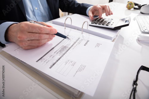 Businessperson Checking Invoice With Calculator