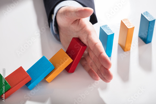 Businessperson Stopping Dominoes From Falling On Desk