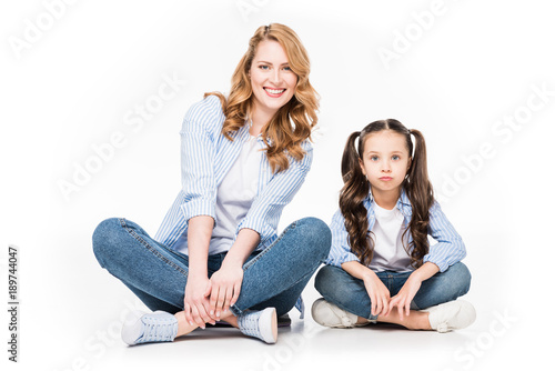 portrait of smiling mother and daughter in denim clothing looking at camera isolated on white