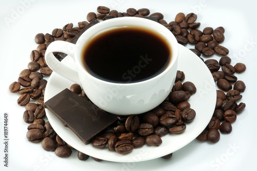 White cup of coffee with a bunch of coffee beans and pieces of chocolate on a white background