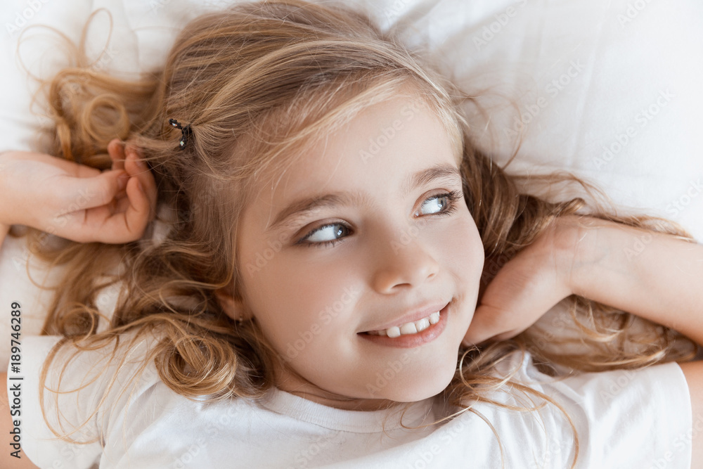 top view of smiling adorable child lying on bed and looking away top view of smiling adorable child lying on bed and looking away