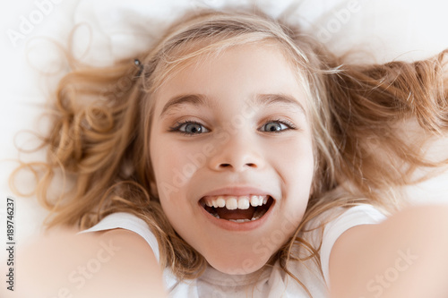 top view of laughing adorable child lying on bed and looking at camera