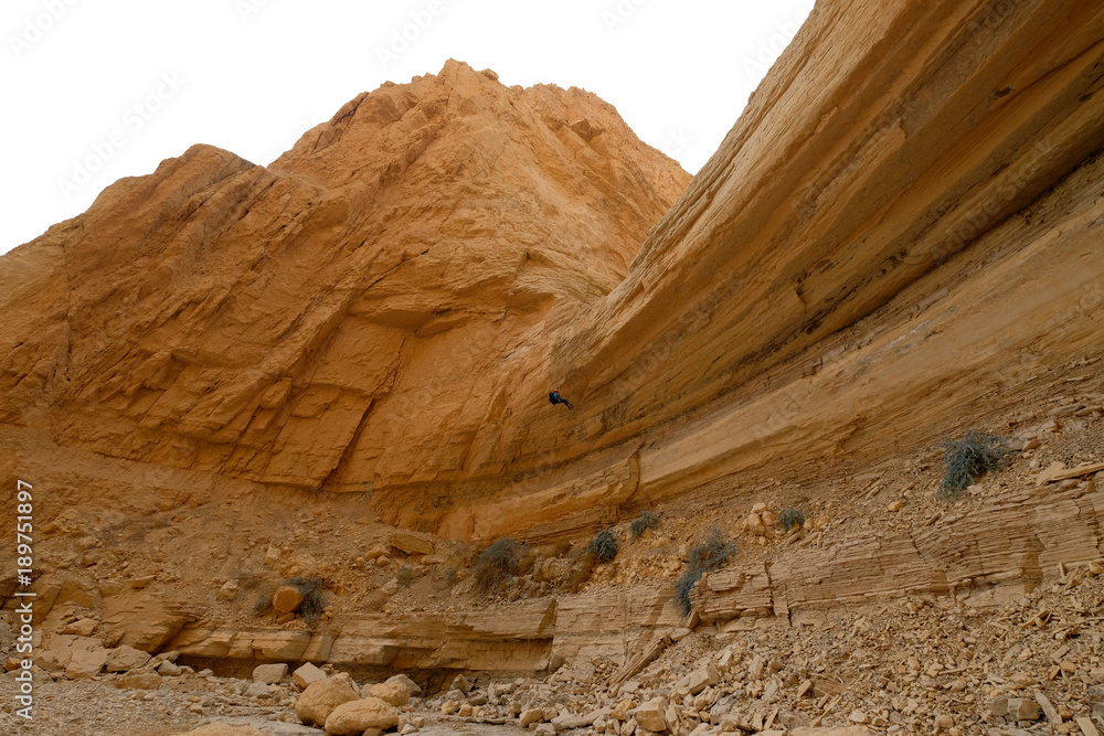 Climber abseiling down from rock cliff in dry wadi in Judea desert. Climber abseiling down from rock cliff in dry wadi in Judea desert.