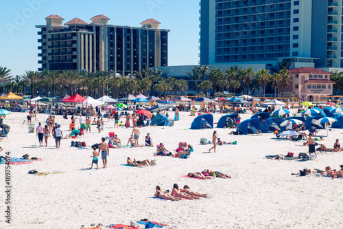Beach holiday destination scene, crowded tropical sandy beach of Clearwater beach Florida, people sun tanning, relaxing and having fun on the beach, holiday hotel resorts on background