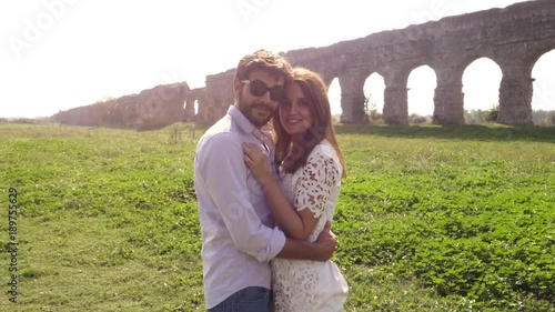 Come with me. Young beautiful girl with hat hugs man boyfriend posing for photo in front of roman aqueduct arches in parco degli acquedotti park ruins in rome romantic lovely couple slow motion photo