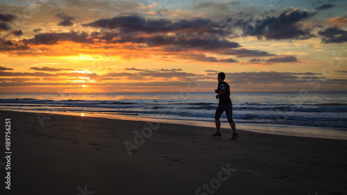 Woman is running by the beach at sunrise.
