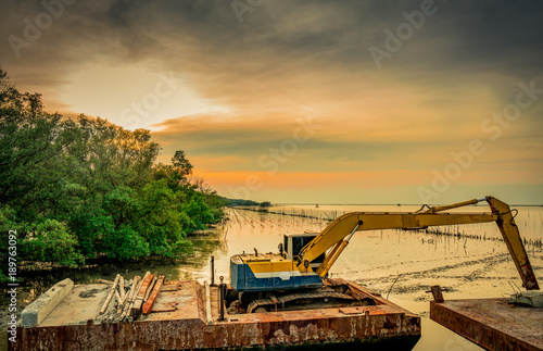 The backhoe is digging along the sea shore near the mangrove forest to place the pipe. Beautiful clouds and sky at construction site