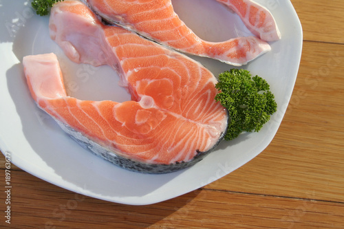 Fresh uncooked salmon fish slices with parsley on a plate on wooden background.