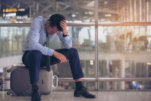 Businessman sitting on luggage at the  terminal airport alone, unhappy trip by delay flight. Insurance and transportation concept.