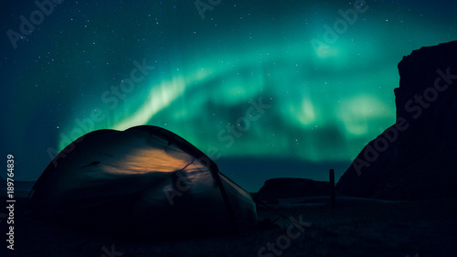 Camping under the northern sky. Northern lights dancing above small tent.