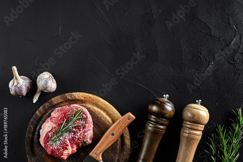 Piece of beef tenderloin, with knife for cutting and chopping meat, spices were cooking - rosemary, pepper, salt, garlic. On old wooden board on stone black table. photo