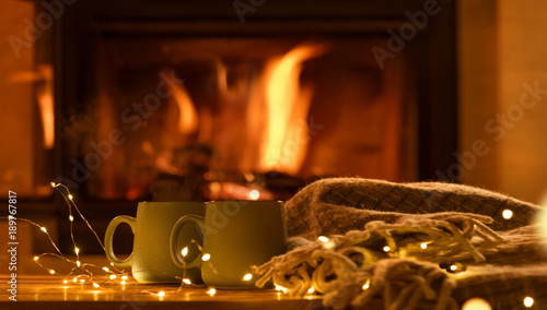 Steam from cups with hot cocoa on the fireplace background.   Decoration garlands of lights . 