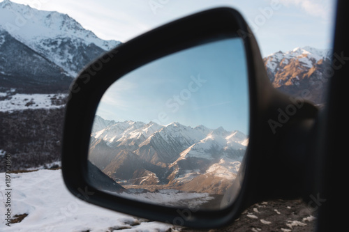 Reflection of a beautiful mountain landscape at sunset in the side mirror of the rear view.