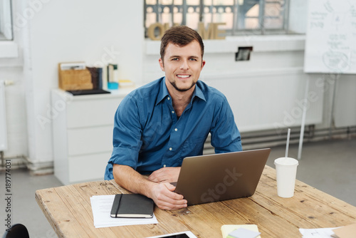 Young cheerful man working with laptop