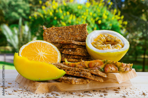 Outdoor view of granola bars with cereals over a wooden table, orange and passion fruit on blurred nature background photo