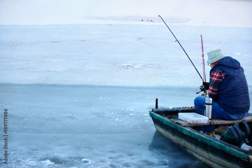 Back view o fisherman in boat while fishing in winter Back view o fisherman in boat while fishing in winter