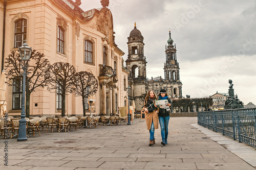 Two charming cheerful women are walking with a map along Dresden Street  Germany. The concept of love and friendship in travel